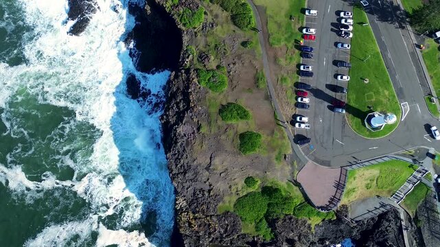 Landscape bird's eye view of rocky headland coastline and Kiama blowhole carpark with lighthouse cars parked ocean sea main town street South Coast travel tourism