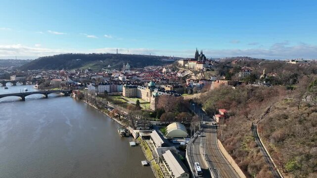 Prague, Czechia, December 2022. Drone gradually pulls away from the The Straka Academy on the banks of the Vltava river with Prague Castle and Petrin hill in the distance.