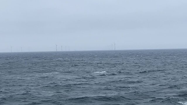 Offshore windmill windfarm turbine energy electricity generation wind park. Electric harvest in water ocean sea at the coastline. Global warming and climate change measure. Clean green sustainable