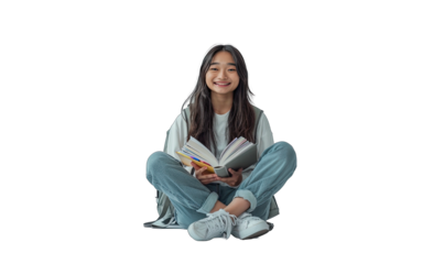 Young woman is sitting on the floor with her legs crossed, holding an open book and smiling. She is wearing casual clothing and has a backpack next to her