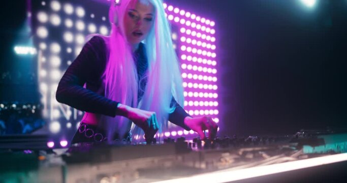 Electronic Dance Music Concert at a Nightclub: Energetic Female Star DJ Performs Live on Stage, Using Turntables to Mix Techno, Trance and House Tunes. Cinematic Handheld Footage