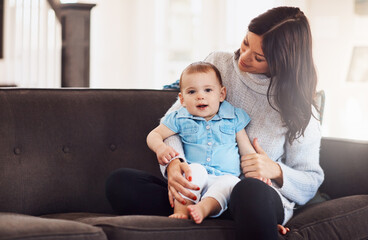 Family, mother and baby on sofa in living room, holding hands for love and embrace for support. Smile, motherhood and toddler with woman together, hug and play by sitting for relationship at home