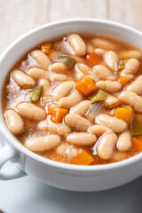 White beans soup with vegetables in white bowl on wooden table. Close up