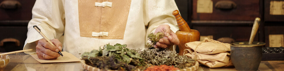 Apothecary in traditional clothes making recipe from dried herbs in drug store