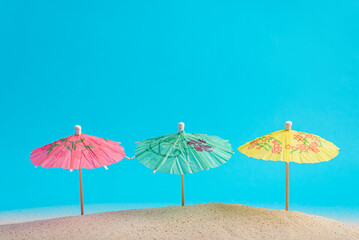 Colorful cocktail umbrellas on sea sand, blue background. Vacation concept. Summer background.