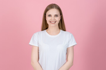 Fototapeta premium Portrait of attractive happy caucasian young blonde woman in casual white t-shirt isolated on pink studio background. She looks at the camera. Successful and friendly.