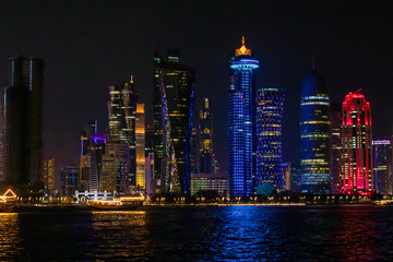 Obraz premium The city skyline is illuminated at night, featuring a boat in the foreground