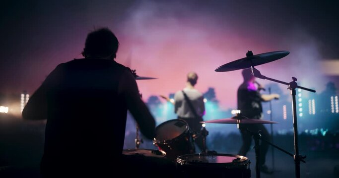 Energetic Drummer Entertaining the Concert Crowd Together with a Creative Rock Band. Famous Headliners Performing a Live Music Performance at an Open Air Festival at Night. Back View