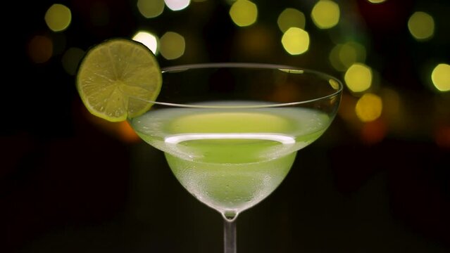 Closeup lime alcoholic cocktail slowly rotating with lemon slice decor on the top