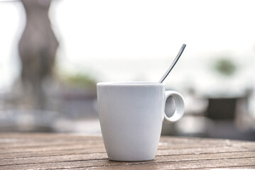 White cup of coffee with spoon on the table outdoors. Selective focus