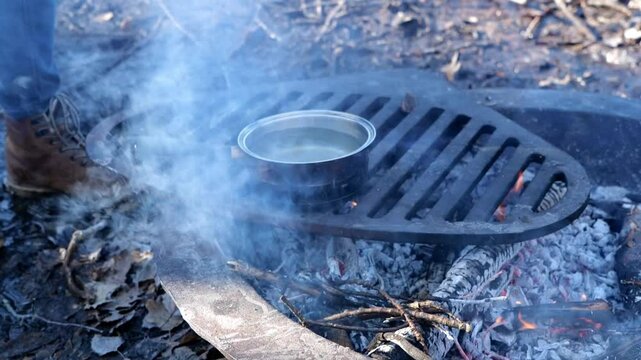 Woman Making Hot Spiced Tea in a Pot of Boiling Water Over a Campfire while Camping in Michigan
