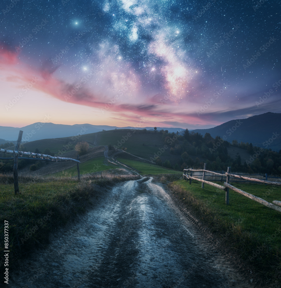 Wall mural milky way, rural road, fence, green hills in mountains at night