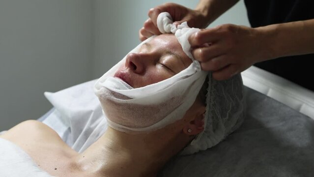 Middle aged female receiving facial anti aged massage in beauty salon. Skincare concept. Cosmetology specialist making facial lifting massage, washing face with napkin after procedure	