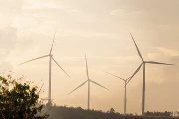 Fototapeta premium Wind turbines on a hillside against an orange sky at sunset, evoking a serene and peaceful atmosphere. Ideal for promoting renewable energy and environmental sustainability.