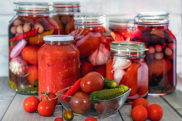 Marinated tomatoes with onions, garlic, and spices in a glass jar, on a wooden table with, an unusual background. Homemade food.