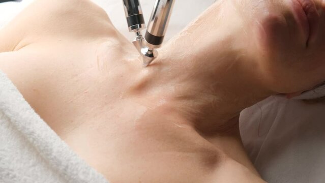A woman undergoes a microcurrent procedure from a cosmetologist, close-up of her neck.