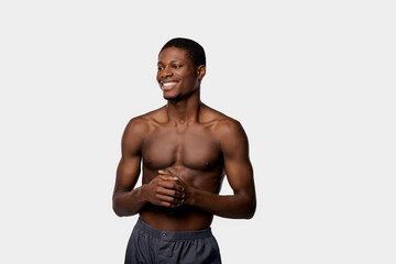 An African American man blissfully smiles, bare-chested with hands clasped together in a studio setting against a white backdrop.