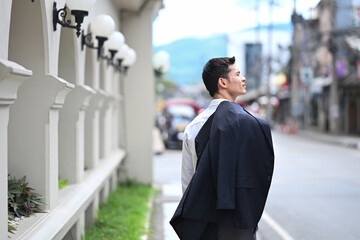 Back view of elegant businessman looking away while walking on the sidewalk in a city street