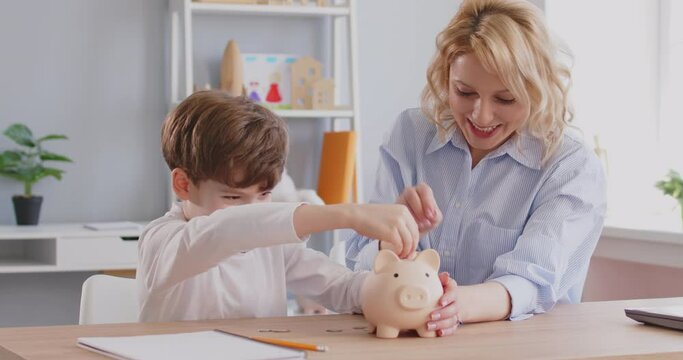 Happy parent and child saving up money together. Cheerful, joyful, smiling little boy and his mother put coins in a piggy bank and give each other a high five