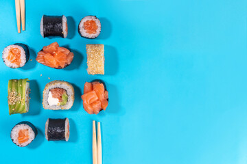 Creative  Japanese seafood sushi set background containing sushi rolls, maki, gunkans with chopsticks on high-colored bright blue background