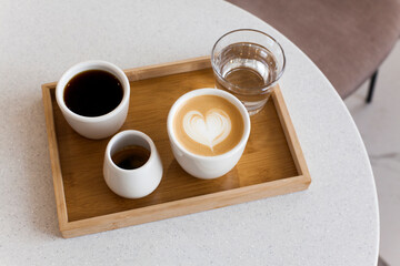 Coffee set on white cafe table. Cappuccino with heart shaped latte art, black filer drip coffee,...