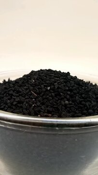 Black cumin seeds or black caraway seeds in a glass bowl isolated rotating on white background in the center frame, close up vertical video