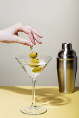 Female hand holds glass of martini cocktail with olives