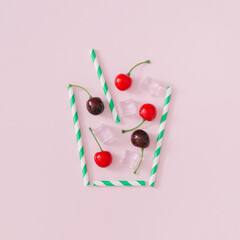 Fototapeta premium Creative layout made of red cherries, ice cubes and drinking straw on light pink background. Minimal cocktail concept. Summer drink composition. Trendy summertime party idea. Summer aesthetic.