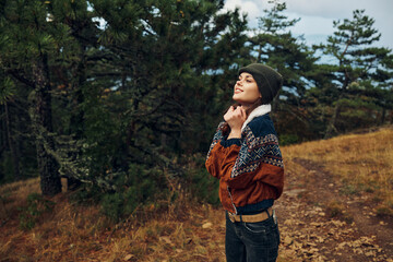 A contemplative woman standing on a forest path with her hands on her head, surrounded by nature and solitude