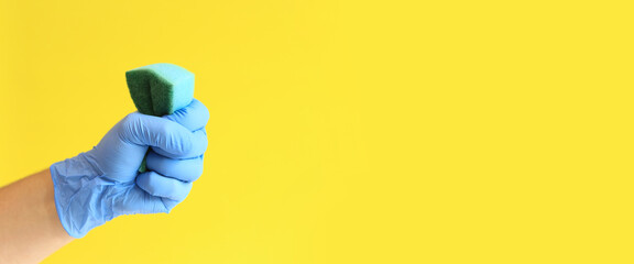 Man's hand in a blue latex glove with a dishwashing sponge. Blue sponge in hand, wet cleaning of the room, yellow background. Cleaning. Wash the dishes. Cleaning service, cleaner