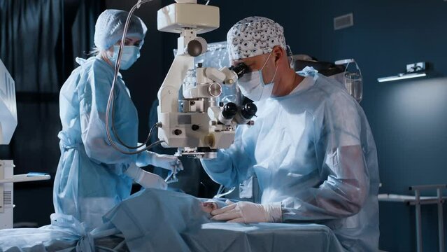 A male doctor performs a high-precision operation. An ophthalmic surgeon sits in front of a microscope and performs an operation. Femtolaser cataract surgery.