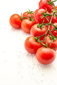 Ripe cherry tomatoes with water drops on white wooden surface in the upper right corner of the photo. Vertical orientation of the photo. Close-up of cherry tomatoes.