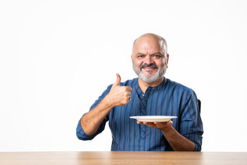 Concept showing Indian asian retired senior old man with empty ceramic plate, holding, presenting...