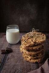 Chocolate chip cookies on table with chocolate and milk on dark brown background 