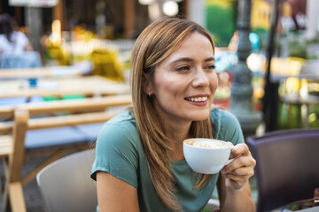 Stylish young woman drinking coffee at the cafe, looking away. Woman enjoying cappuccino in a cafe.