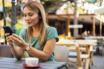 Portrait of beautiful young woman using smartphone while enjoying morning on outdoor terrace in cafe or coffee shop, copy space. - Powered by Adobe