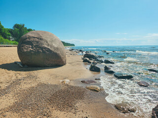 “A serene beachscape showcasing a large boulder and scattered rocks along the water’s edge...