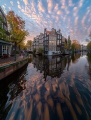 Obraz premium Dutch Canal Reflections at Sunset - A picturesque scene of a canal in Amsterdam, Netherlands, with traditional Dutch architecture reflecting in the calm water at sunset.
