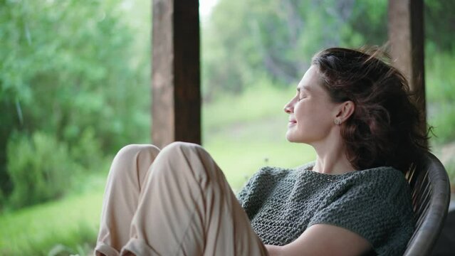 A young Caucasian woman enjoying the fresh air while sitting on the terrace of a country house on a rainy day
