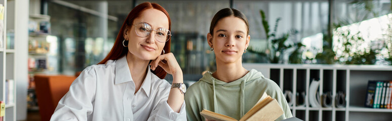 Redhead woman tutors teenage girl in library, both engrossed in book