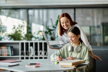 A redhead woman teaches a teenage girl at a desk, both focused on a laptop during an after-school...