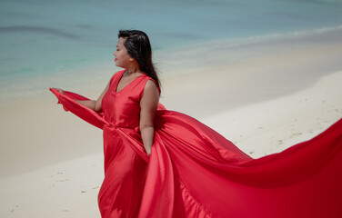 Lady in red satin flying dress flowing at the beach