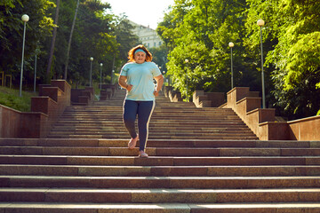 Overweight happy smiling fat woman having sport training in the summer city park running outdoors....
