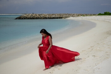 Lady in red satin flying dress flowing at the beach