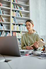 A teenager engrossed in modern education, surrounded by books and a laptop, diligently doing...