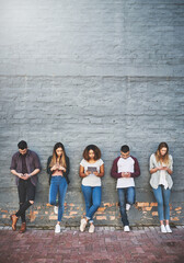 Obraz premium People, row and online outdoor with technology for study break, social media and campus friends. College, students and wall background with texting for communication, digital interaction and search.