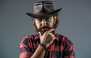 Cowboy style in a plaid shirt. Leather cowboy hat. Handsome young man adjusting his cowboy hat....