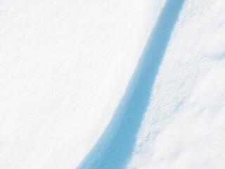 Beautiful winter background with snowy ground. Natural snow texture. Wind sculpted patterns on snow surface. Closeup top view with copy space.