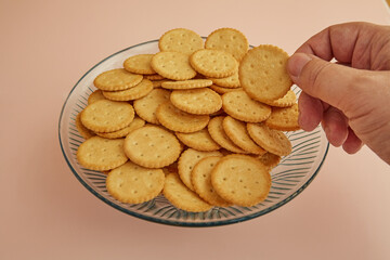 A hand takes a cracker from a vase of cookies on a pink background, close-up, freshly baked cookies, delicate cookies..