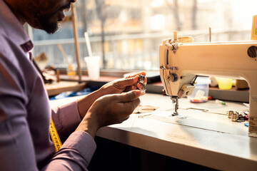 Male fashion tailor working on the sewing machine for the suit design in his workshop.